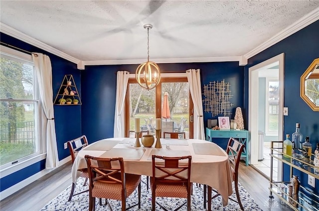 dining area featuring light wood-style flooring, an inviting chandelier, ornamental molding, a textured ceiling, and baseboards