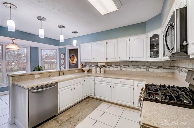 kitchen featuring a peninsula, a sink, light countertops, appliances with stainless steel finishes, and backsplash