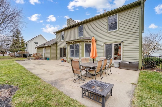 back of house featuring a patio, a chimney, a lawn, fence, and a fire pit