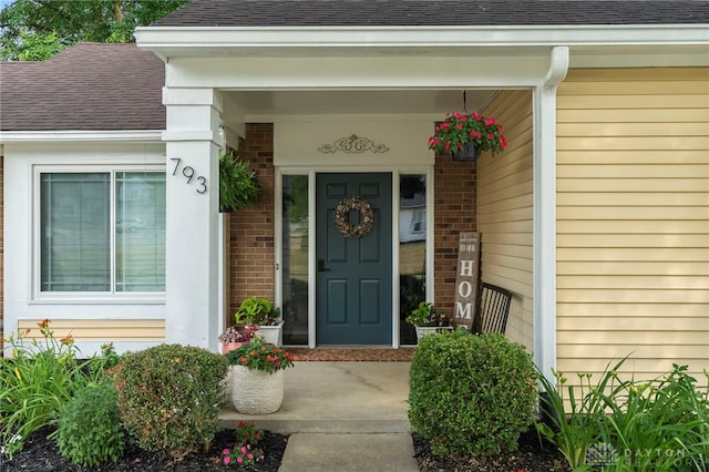 entrance to property with a shingled roof and brick siding