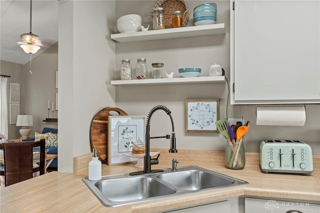 kitchen with hanging light fixtures, vaulted ceiling, light countertops, open shelves, and a sink