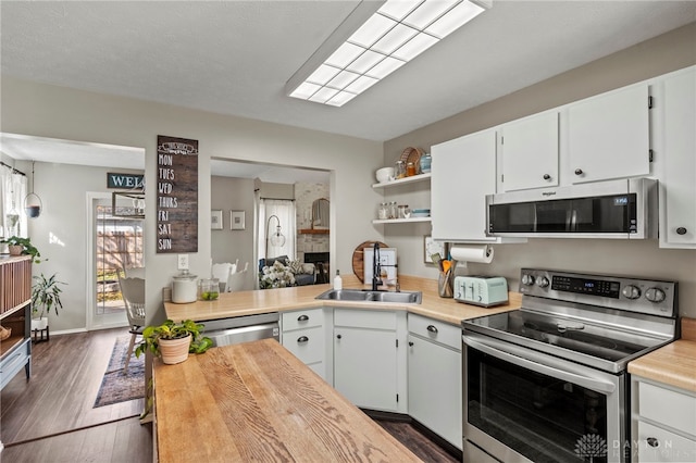 kitchen with dark wood-style flooring, open shelves, appliances with stainless steel finishes, a sink, and wood counters