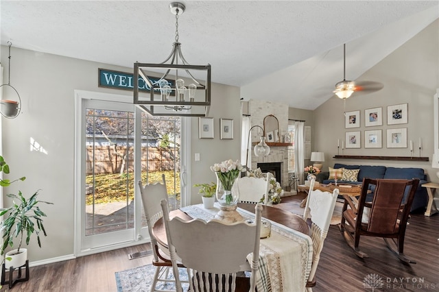 dining space featuring lofted ceiling, ceiling fan, a textured ceiling, a fireplace, and wood finished floors