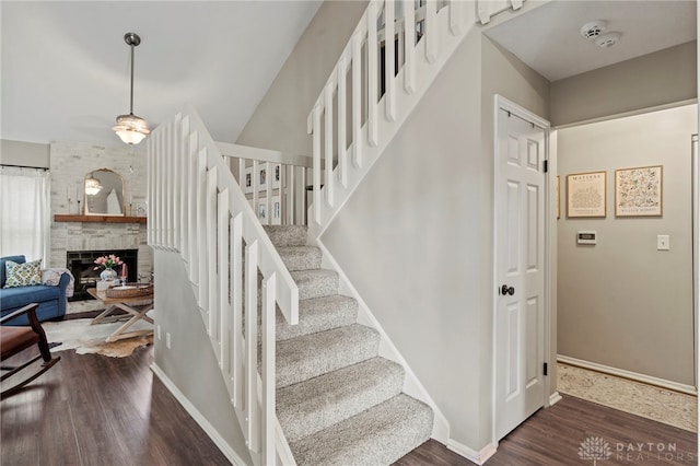 staircase with a large fireplace, baseboards, and wood finished floors