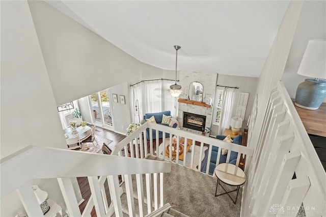 staircase featuring high vaulted ceiling, a stone fireplace, and wood finished floors