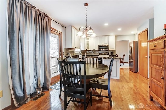 dining room with light wood-type flooring, an inviting chandelier, and visible vents