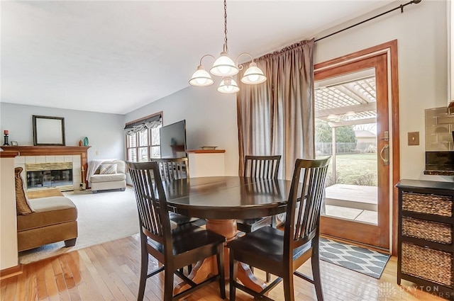 dining room featuring light wood finished floors, a tile fireplace, and a notable chandelier