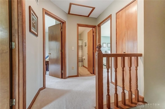 corridor featuring attic access, light carpet, and baseboards