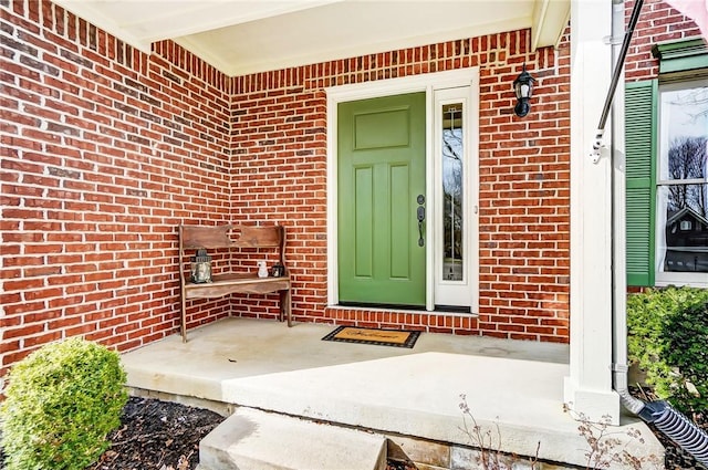 view of exterior entry with a porch and brick siding