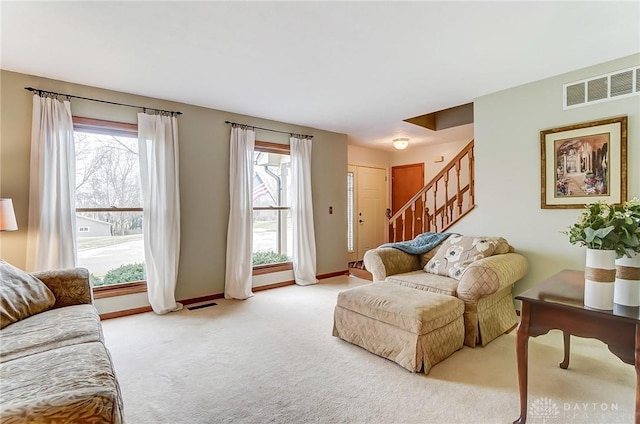 living area with stairway, baseboards, visible vents, and light colored carpet