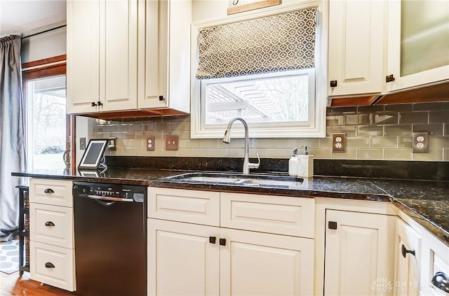 kitchen with a sink, white cabinetry, black dishwasher, backsplash, and dark stone counters