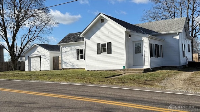 view of front of home featuring a front yard, roof with shingles, fence, and a detached garage