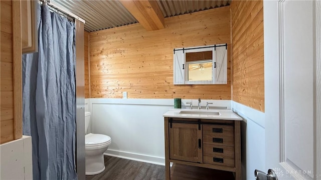 bathroom featuring beamed ceiling, wooden walls, toilet, and vanity