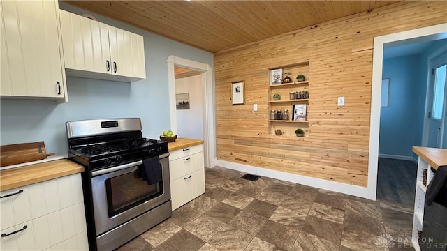 kitchen with wooden walls, wood ceiling, stainless steel gas range, white cabinetry, and wooden counters