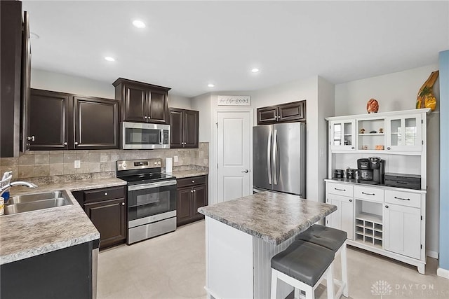 kitchen with dark brown cabinetry, appliances with stainless steel finishes, a breakfast bar, a sink, and backsplash