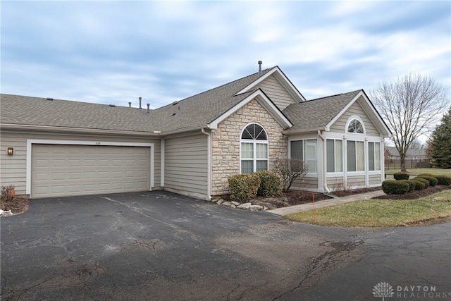 ranch-style house with a shingled roof, stone siding, an attached garage, and aphalt driveway