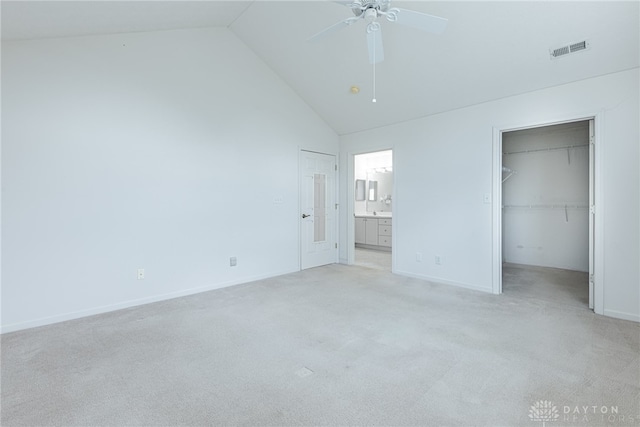 unfurnished bedroom featuring visible vents, connected bathroom, light colored carpet, a walk in closet, and high vaulted ceiling