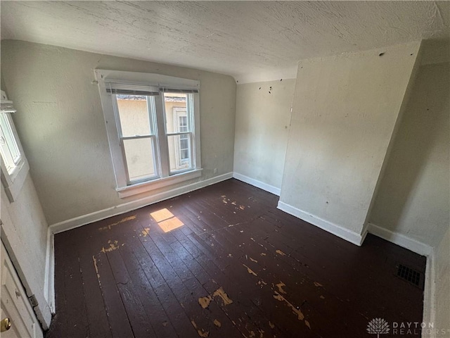 empty room featuring a textured ceiling, wood-type flooring, visible vents, and baseboards