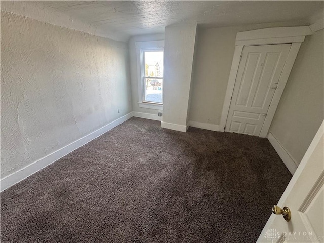 unfurnished bedroom featuring dark colored carpet, a textured wall, a textured ceiling, and baseboards