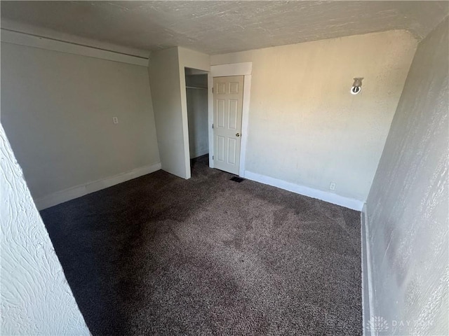 empty room featuring visible vents, dark carpet, a textured ceiling, and baseboards