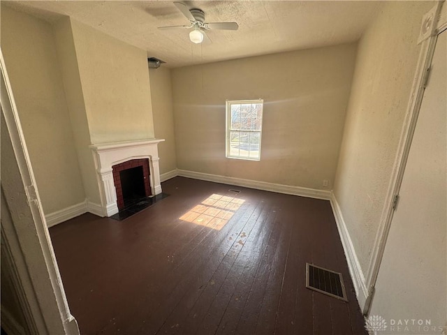 unfurnished living room with dark wood-style floors, a tiled fireplace, visible vents, and baseboards