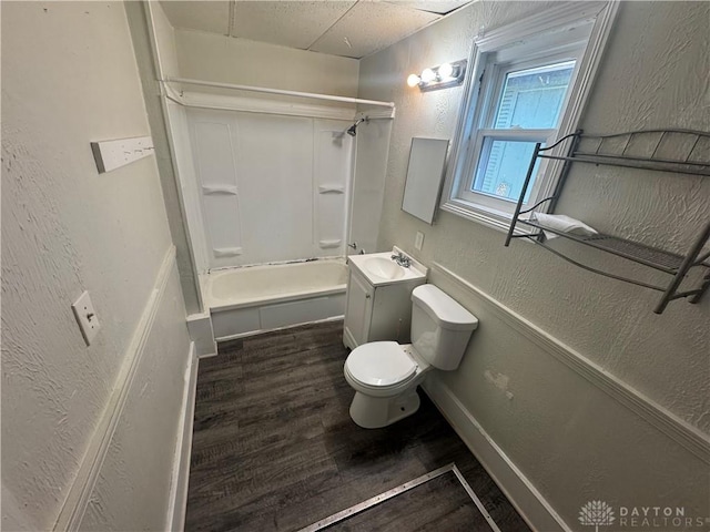 bathroom featuring a textured wall, shower / bathing tub combination, toilet, vanity, and wood finished floors