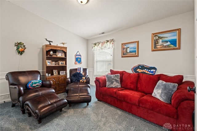 carpeted living room with lofted ceiling, a wainscoted wall, and visible vents