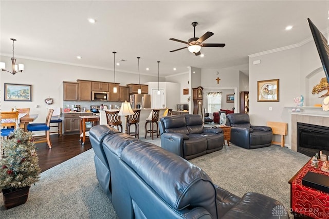 living room featuring ornamental molding, dark wood-style flooring, ceiling fan with notable chandelier, a fireplace, and recessed lighting