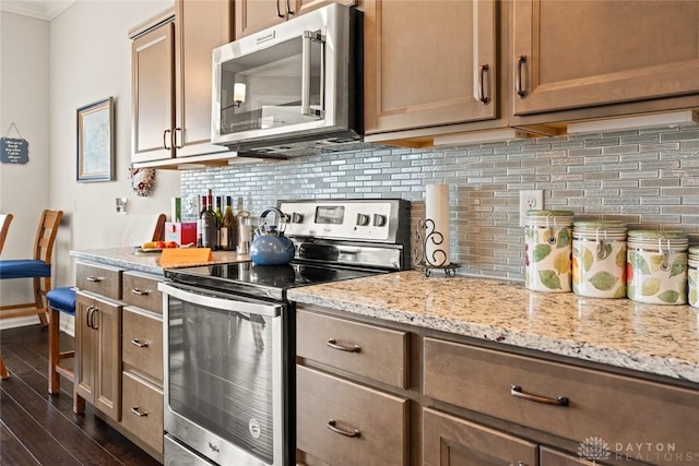 kitchen featuring light stone counters, ornamental molding, appliances with stainless steel finishes, decorative backsplash, and dark wood finished floors