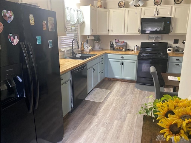 kitchen featuring light wood-style flooring, butcher block counters, a sink, white cabinets, and black appliances