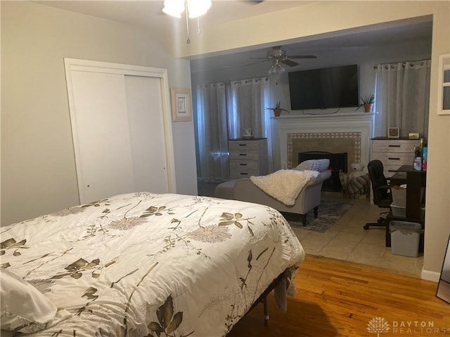 bedroom with a closet, a tiled fireplace, wood finished floors, and a ceiling fan