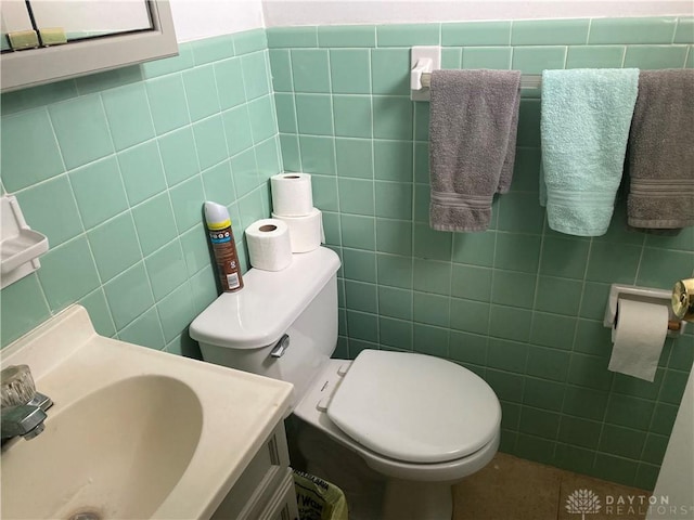 half bath with toilet, a sink, and tile walls