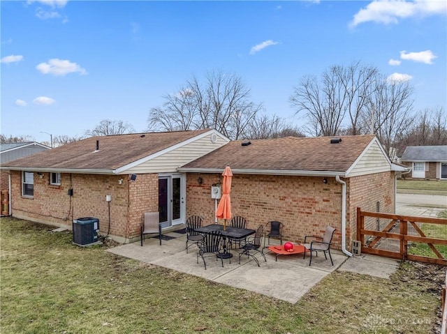 rear view of house with a yard, brick siding, a patio, and roof with shingles