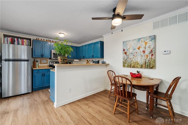 kitchen with ornamental molding, stainless steel appliances, light countertops, light wood-type flooring, and blue cabinetry