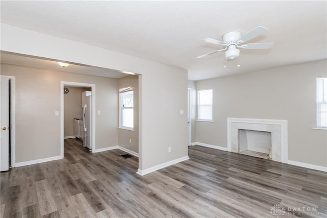 unfurnished living room with ceiling fan, a fireplace, baseboards, and wood finished floors