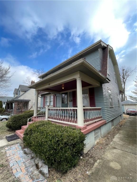 view of property exterior with covered porch and an outbuilding