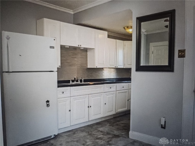 kitchen featuring a sink, white cabinets, ornamental molding, freestanding refrigerator, and dark countertops