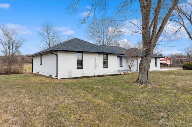 view of side of home with roof with shingles, brick siding, and a lawn