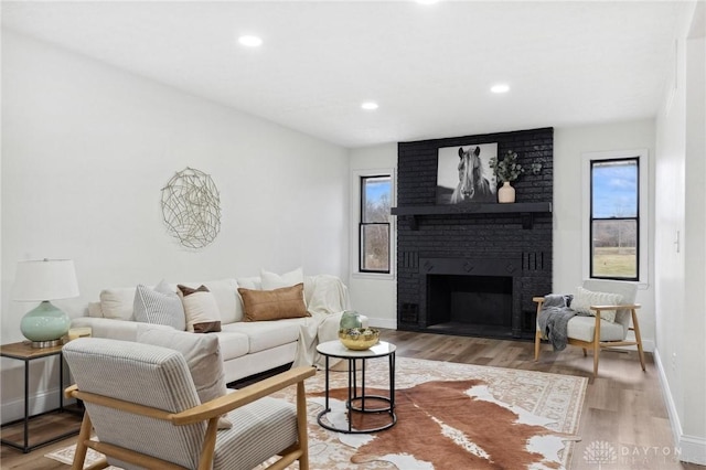 living room featuring a brick fireplace, plenty of natural light, baseboards, and wood finished floors