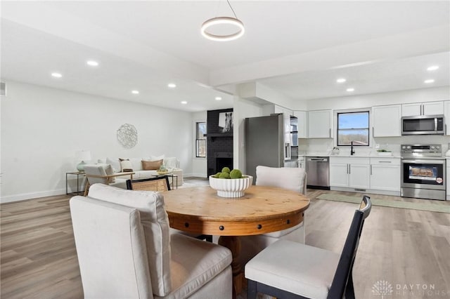 dining area with recessed lighting, a brick fireplace, light wood-style flooring, and baseboards