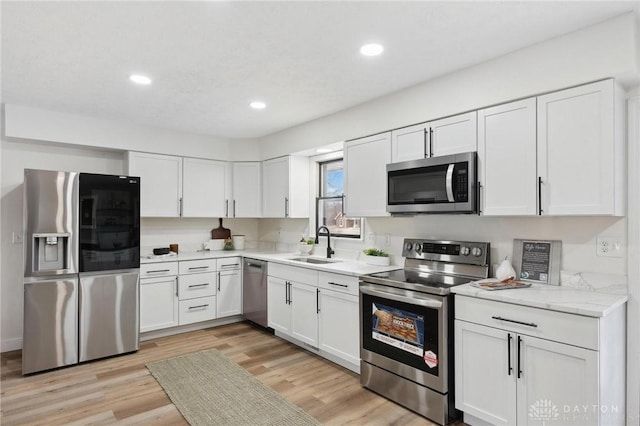 kitchen featuring stainless steel appliances, light wood-type flooring, white cabinetry, and a sink