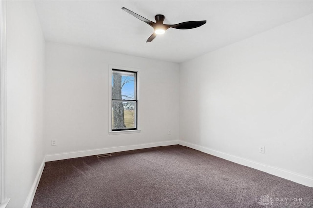 unfurnished room featuring baseboards, visible vents, dark carpet, and a ceiling fan