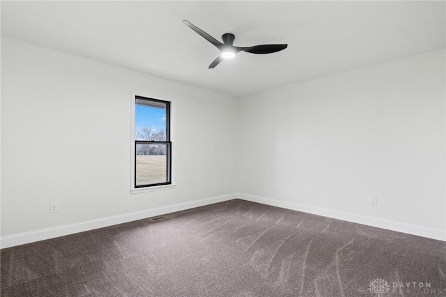 empty room featuring dark colored carpet, a ceiling fan, and baseboards