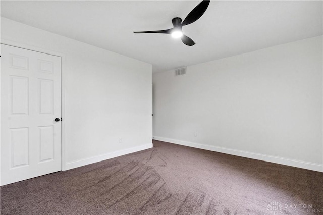 empty room featuring baseboards, visible vents, dark carpet, and a ceiling fan