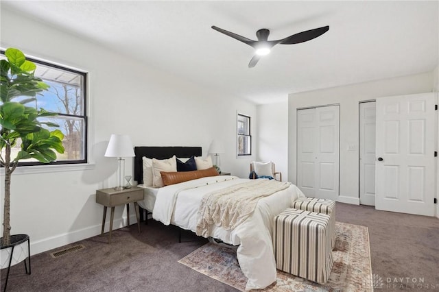 carpeted bedroom with multiple closets, visible vents, ceiling fan, and baseboards