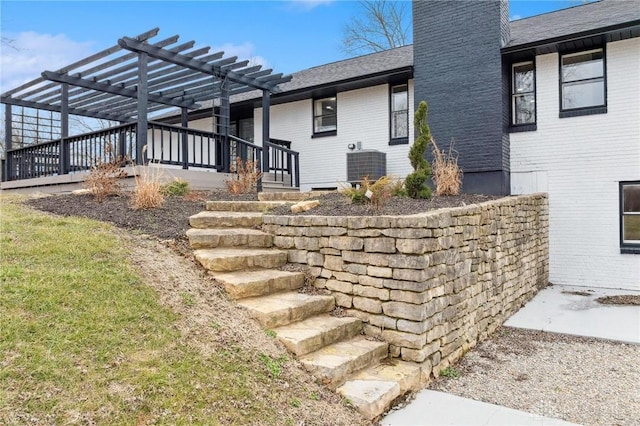 view of property exterior featuring central air condition unit, a shingled roof, a chimney, and a pergola