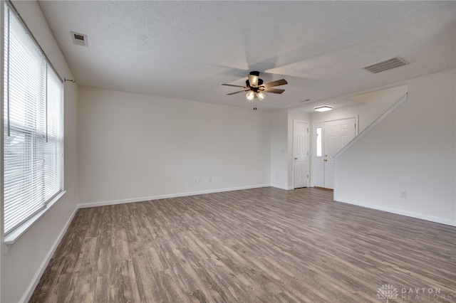 empty room with a textured ceiling, wood finished floors, visible vents, and baseboards