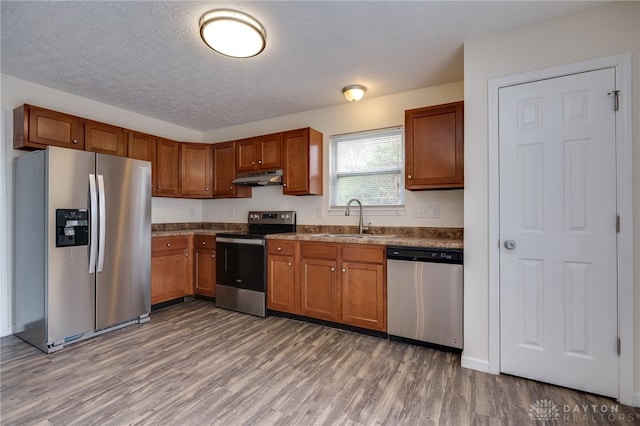 kitchen featuring stainless steel appliances, a sink, light wood-style flooring, and under cabinet range hood