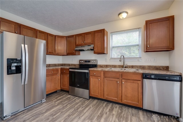 kitchen with appliances with stainless steel finishes, brown cabinetry, a sink, and under cabinet range hood