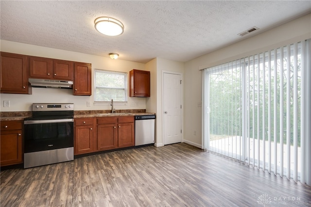 kitchen with visible vents, appliances with stainless steel finishes, brown cabinets, under cabinet range hood, and a sink